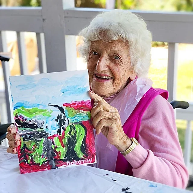 A smiling older woman holding up her colorful painting