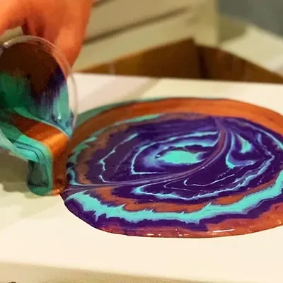 Paint being poured from a cup onto a canvas in rings of color