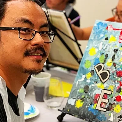 A man smiling beside his abstract painting at a workshop