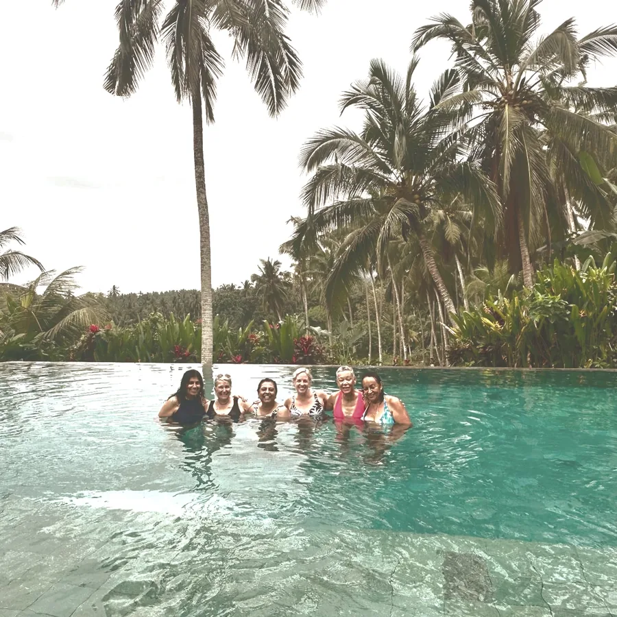 Women relaxing together in a pool framed by palm trees