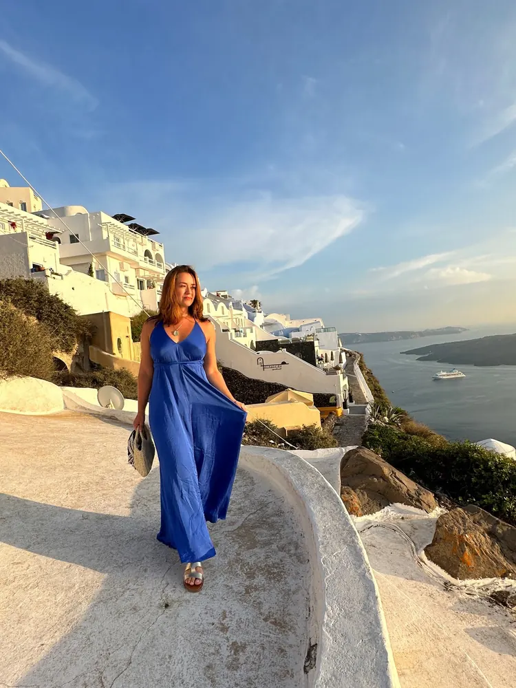 Ana in a long blue dress above the sea in Santorini