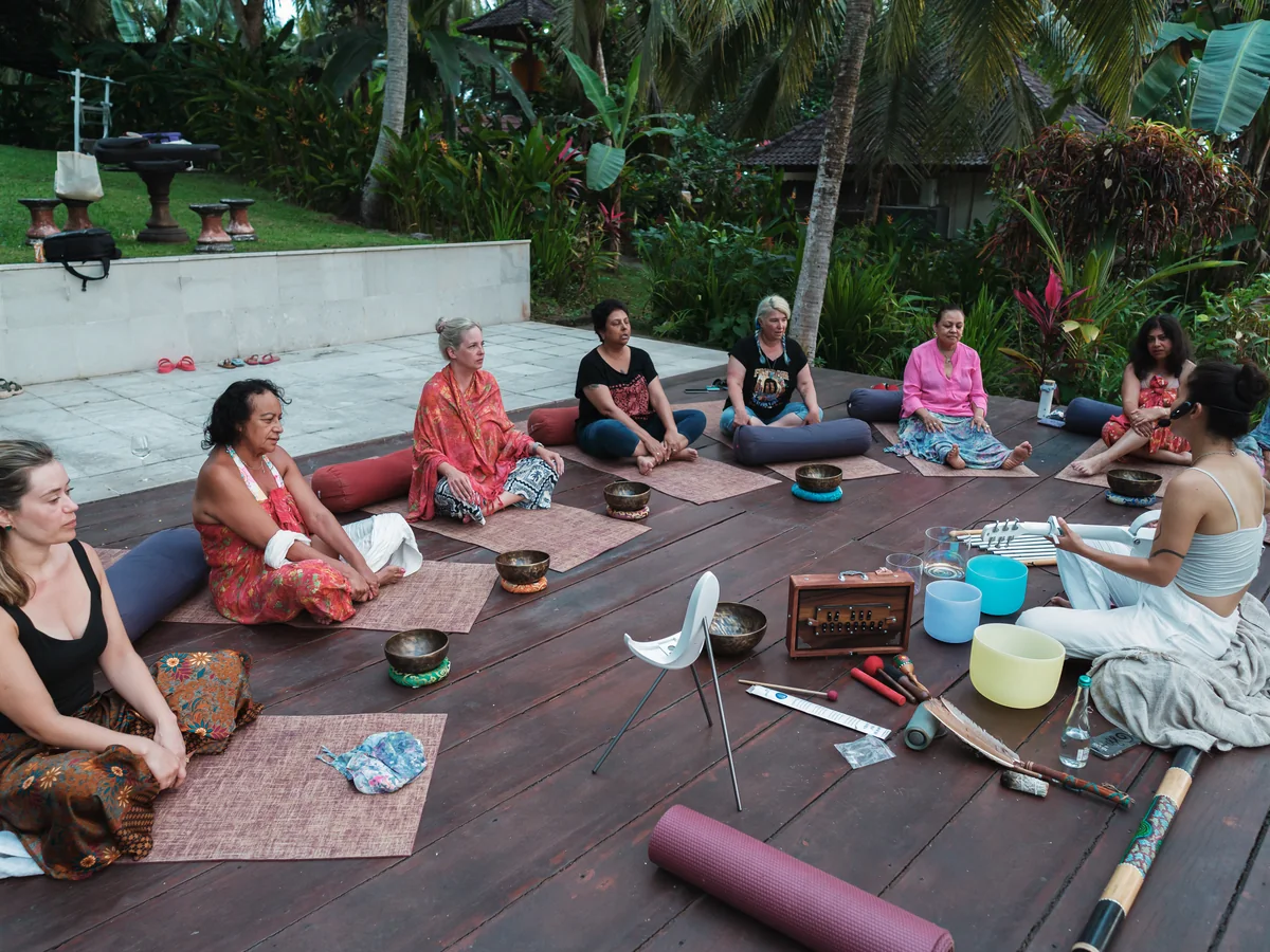 Women sitting in a circle on a wooden deck during a sound healing ceremony with singing bowls