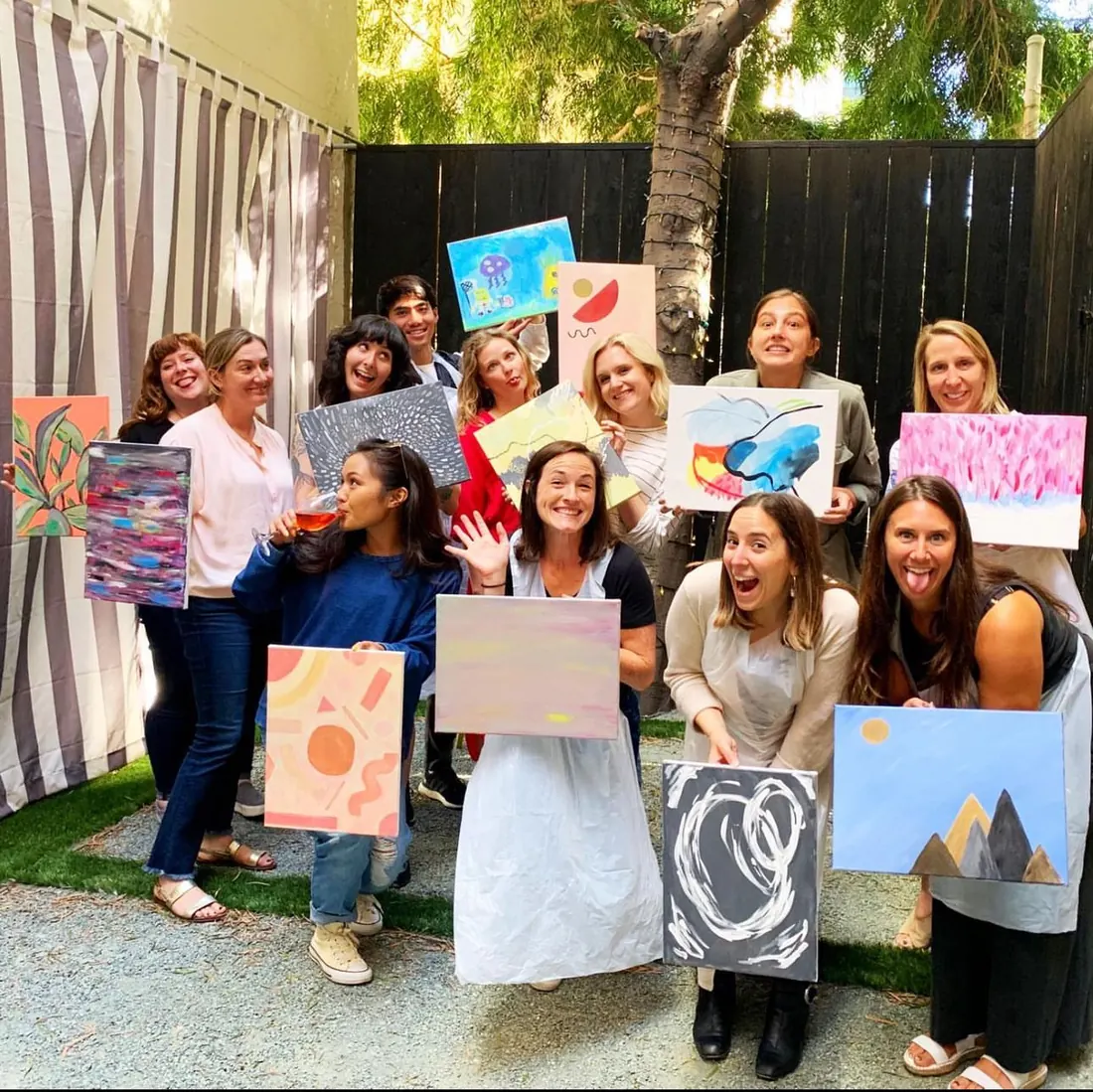 A cheerful group holding up the paintings they made at one of Ana's workshops